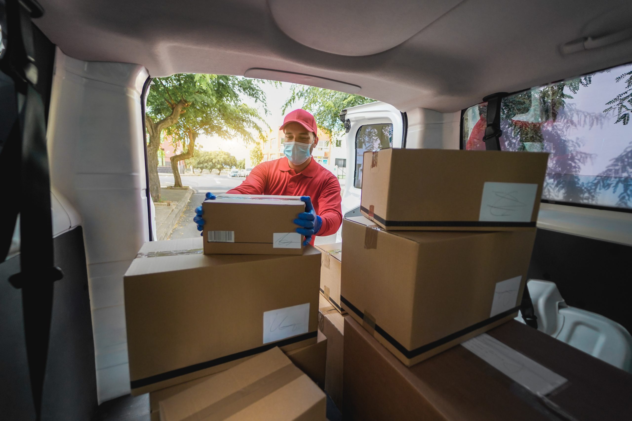 Delivery man picking up cardboard box from van during coronaviru